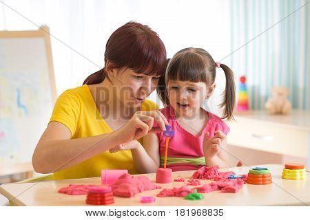 Cute kid girl and mother playing with kinetic sand at home