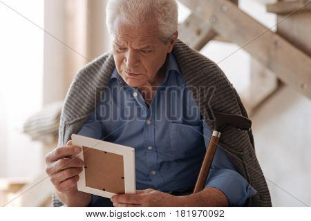 I will always love you. Depressed cheerless unhappy man looking at the old photo and remembering his wife while grieving about her