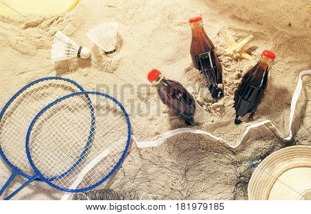 Summer background. Three bottles of cool drink with items for beach entertainment on sand top view