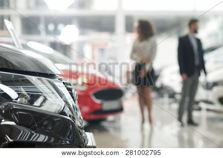 Close Up Of Black Car Headlight. Modern Showroom With Expensive Automobiles. People Standing In Car 
