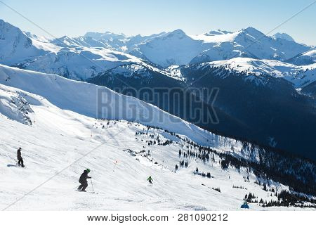 Skiers On A Hill At The Top Of Blackcomb, 7th Heaven, With A View Looking Toward Whistler On A Sunny
