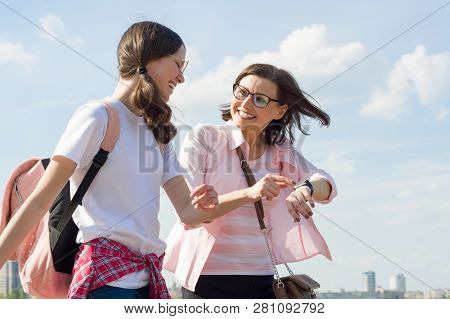 Mom And Teen Daughter Walking Along City Street. Mother Showing Her Daughter Clock On The Hand, Wome