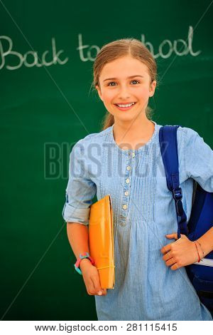 Back to school.. Funny beatifull girl sitting in the clasroom against blacboard. Child in school with book and accessories. Education concept