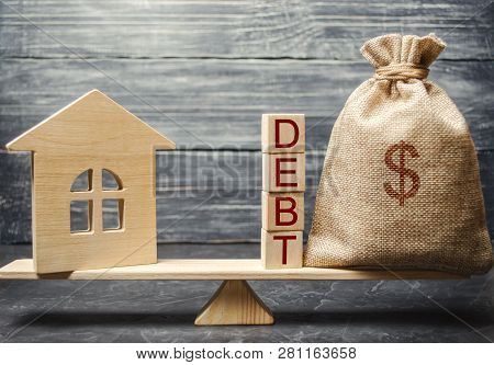 Money Bag And Wooden Blocks With The Word Debt And A Miniature House On The Scales. Payment Of Debt 