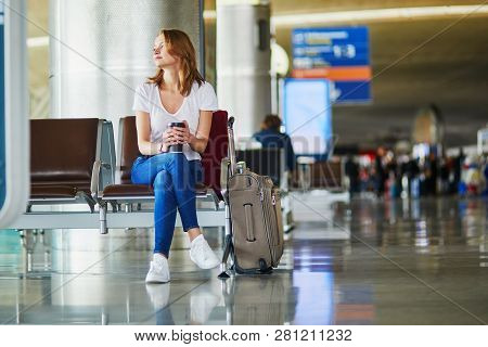 Young Woman In International Airport With Luggage And Coffee To Go, Waiting For Her Flight