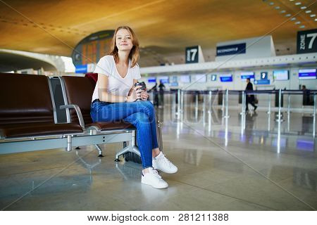 Young Woman In International Airport With Luggage And Coffee To Go, Waiting For Her Flight