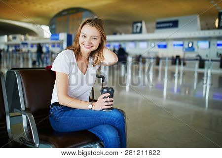 Young Woman In International Airport With Luggage And Coffee To Go, Waiting For Her Flight