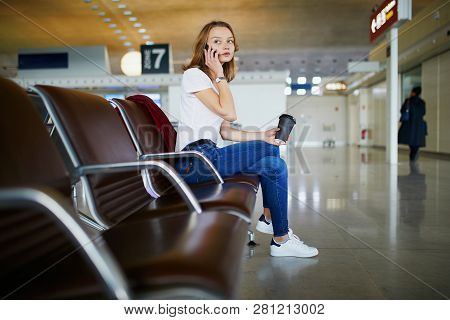 Young Woman In International Airport With Luggage And Coffee To Go, Waiting For Her Flight