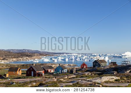 Rodebay, Greenland - July 09, 2018: Colorful Wooden Houses With Icebergs In The Background. Rodebay,