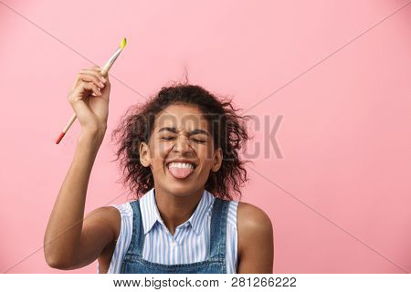 Beautiful young african woman atrist holding a paint brush over pink background