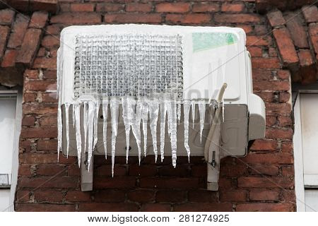 Closeup Of Frozen Air Conditioner On The Brick Wall Covered With Icicles. Thaw, Cooling, Winter Weat