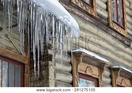 Ice Stalactite Hanging From The Roof With Wooden Wall. Building Covered With Large Icicles. Icicles 