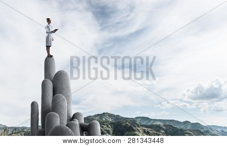 Young Female Doctor With Folder In Hands Satnding On Stone Column