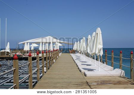 View Of Long Pier With White Chaise-longues And Sunshades