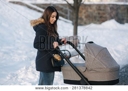 Young Mother Walking With Her Baby In Pram. Beautiful Stoller. Winter Photosession