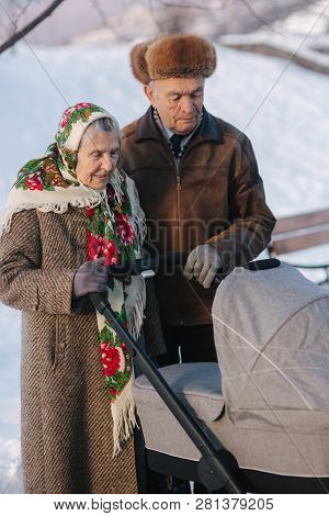 Grand Grandparents Walking With A Baby In Beautiful Pram. Winter Time