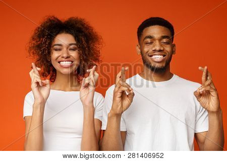 Making Cherished Wish. Young Cheerful African-american Couple With Closed Eyes And Crossed Fingers, 
