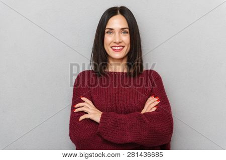 Image of beautiful young woman dressed in burgundy sweater posing isolated over grey wall background.