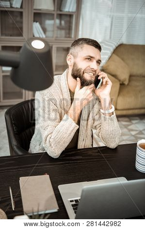 Thoughtful Doubting Man Talking On Smartphone While Leaning On Office Table