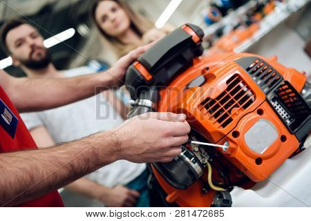Close Up. Salesman In Red Shirt And Baseball Cap Is Showing Couple Of Clients New Leaf Blower In Pow