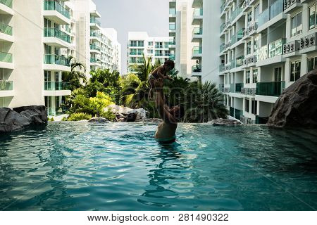 Dad Throws Baby In The Pool On The Background Of Coconut Palms. Happy Active Family Young Father And