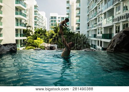 Dad Throws Baby In The Pool On The Background Of Coconut Palms. Happy Active Family Young Father And