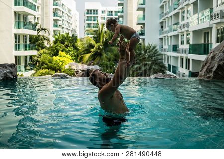 Dad Throws Baby In The Pool On The Background Of Coconut Palms. Happy Active Family Young Father And