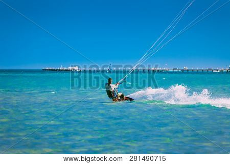 Egypt, Hurghada - 30 November, 2017: The kiter gliding over the Red sea waves. The back side. Breathtaking transparent turquoise water under the clear blue sky. The pier background. Active leisure.
