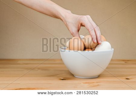 Female Hand Taking One Egg From White Bowl On A Table .