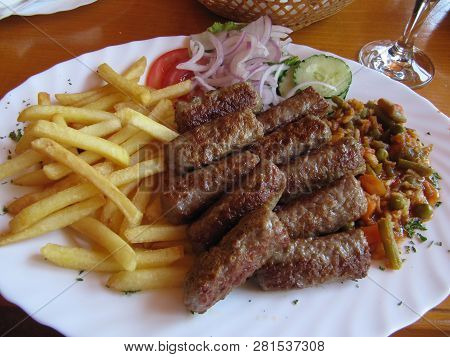 Chevapchichi With Fries And Salad And Vegetables On White Plate. Dish Of Balkan Cuisine.