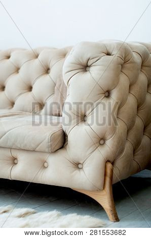 Fragment Of A Beige Sofa With Buttons On Wooden Legs, Living Room