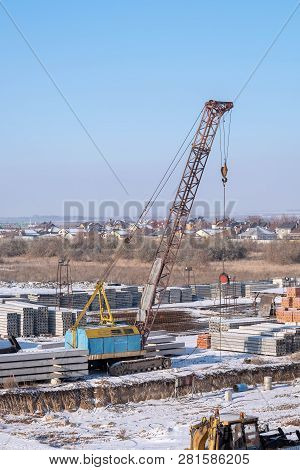 Crawler Crane, Piles And Concrete Slabs At A Construction Site Near A Multi-storey Building. Transla