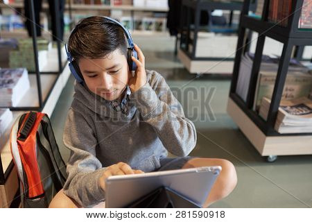 Positive Teenage Boy In Headphones Watching Lection Online In School Library