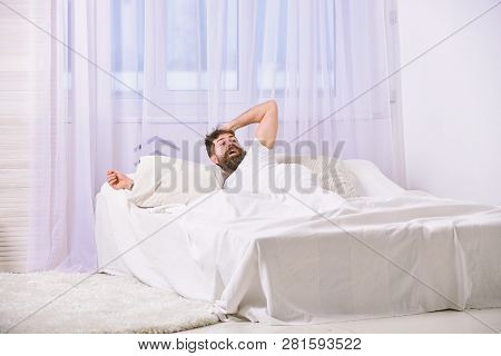 Man In Shirt Laying On Bed Awake, White Curtain On Background. Guy On Shocked Face Waking Up In Morn
