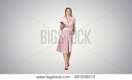 Young Woman In Pink Looking At Mobile Smartphone And Texting Something While Walking On Gradient Bac