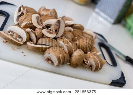 A Pile Of Sliced Chestnut Mushrroms (agaricus Bisporus) On A White Chopping Board
