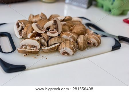 A Pile Of Sliced Chestnut Mushrroms (agaricus Bisporus) On A White Chopping Board