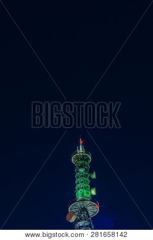 Low Angle Night View Of Large Communication Array Tower Lit Up In Red Lights With Dark Blue Sky In B