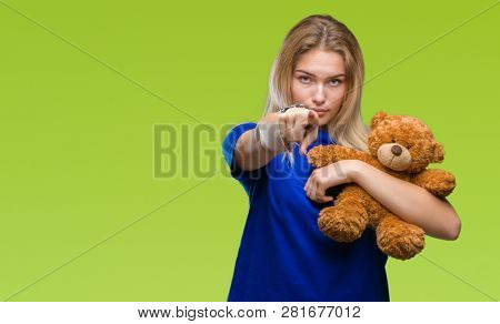 Young caucasian woman holding cute teddy bear over isolated background pointing with finger to the camera and to you, hand sign, positive and confident gesture from the front