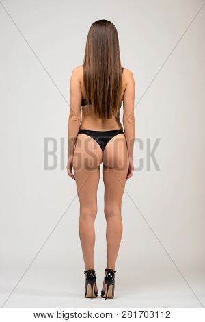 Full Length Portrait Of Beautiful Brunette Women With Slim Figure In Black Bra And Shorts. Back View