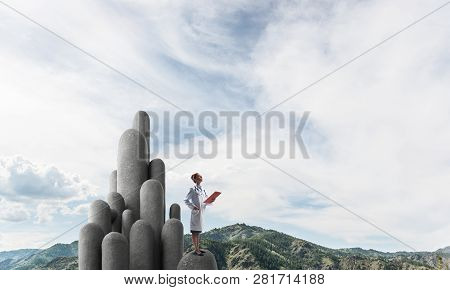 Young Female Doctor With Folder In Hands Satnding On Stone Column