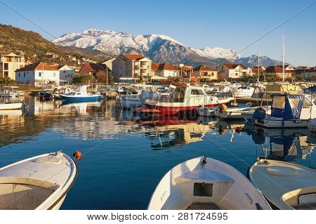 Sunny Winter Day. Fishing Boats In Harbor In Mediterranean Town At Foot Of Snowy Mountains. Monteneg