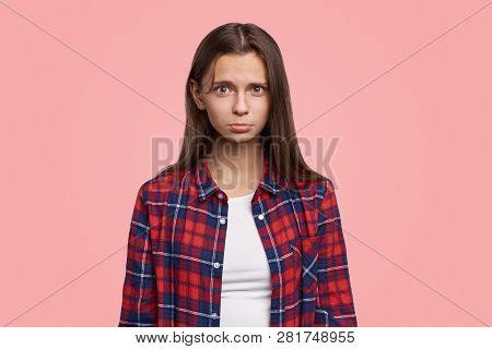 Discontent Miserable Female Looks In Camera, Purses Lips, Being In Low Spirit. Gerl Stands Against P
