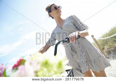 Gorgeous young woman in polka dot dress walking with bicylce on beach