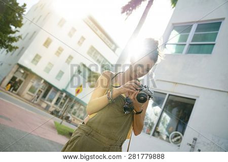 Stylish young woman looking at vintage camera in urban setting