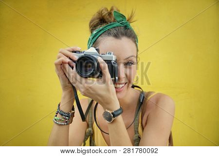 Young stylish woman taking photos outdoors with vintage camera on colored background