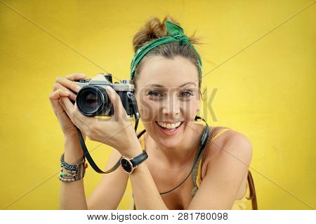 Young stylish woman taking photos outdoors with vintage camera on colored background