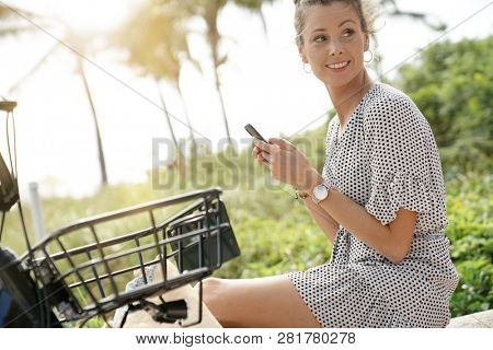 Pretty young woman sitting outdoors with bicylce and cellphone