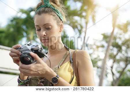 Stylish young woman looking vintage camera surrounded by palm trees