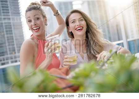 Two attractive funloving friends partying with drinks on rooftop bar in city